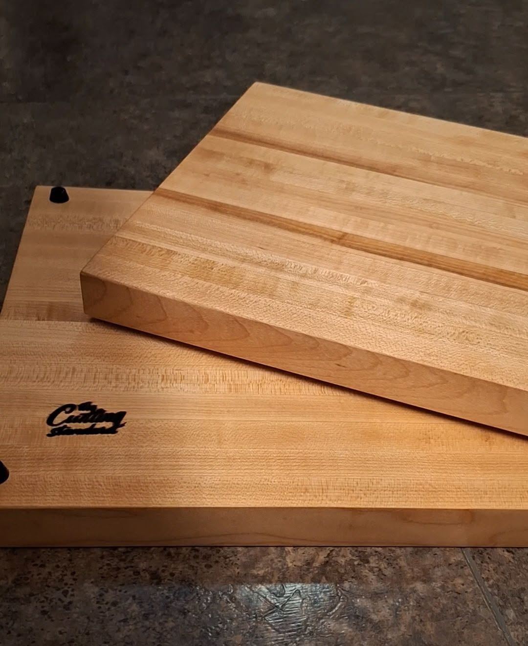 Two stacked hard maple cutting boards with The Cutting Standard logo and black rubber feet